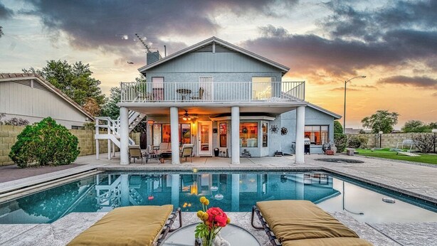Une maison à deux étages avec un balcon, une piscine et des chaises longues.