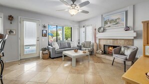 Un salon spacieux doté d’une cheminée, d’un ventilateur de plafond et d’une grande fenêtre.