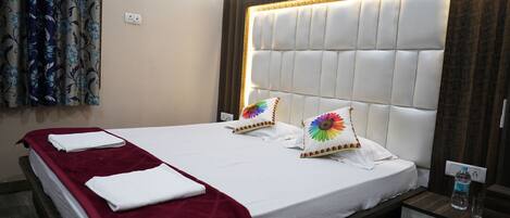 Habitación de hotel con una cama grande, un plaid rojo, dos almohadas con un diseño floral colorido, un cabecero de madera y una mesita de noche con una botella de agua.