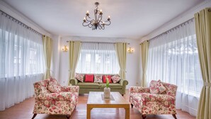 Ein geräumiges Wohnzimmer mit einem grünen Sofa, zwei floralen Sesseln, einem Holztisch und einer Chandelüster.