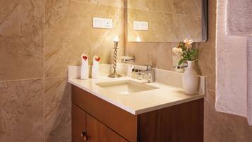 A bathroom with a marble wall, a sink, a mirror, and a vase with flowers.