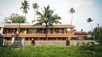 A two-story building with balconies, surrounded by palm trees and greenery.