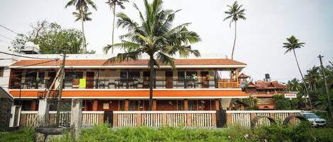A two-story building with balconies, surrounded by palm trees and greenery.