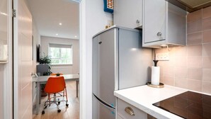A modern kitchen with a built-in refrigerator, a countertop with a stove, and a window providing natural light. - Stylish Brixton Hill Studio with Modern Charm (London)