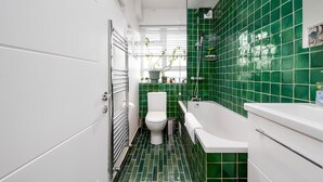 A modern bathroom with a green-tiled shower, a white toilet, and a bathtub. - Stylish Brixton Hill Studio with Modern Charm (London)
