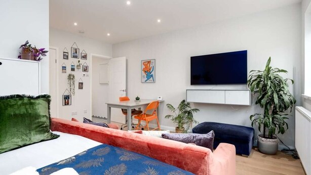 A modern, well-lit room with a bed, a sofa, a TV, and a desk. - Stylish Brixton Hill Studio with Modern Charm (London)