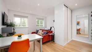 A modern living room with a white sofa, orange chair, and a dining table. - Stylish Brixton Hill Studio with Modern Charm (London)