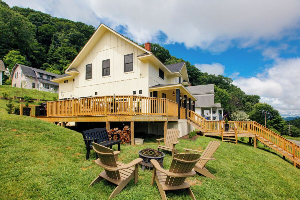 A large house with a wooden deck, outdoor seating, and a fire pit.