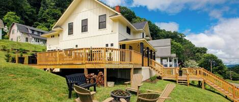 A large house with a wooden deck, outdoor seating, and a fire pit.