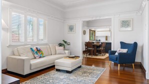 A spacious living room with a white sofa, a blue armchair, and a dining area in the background.