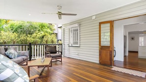A wooden deck with a sofa and chairs, a ceiling fan, and a view of greenery.