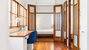 A traditional Japanese-style room with tatami flooring, a low wooden desk with a lamp, and a bed with a futon.