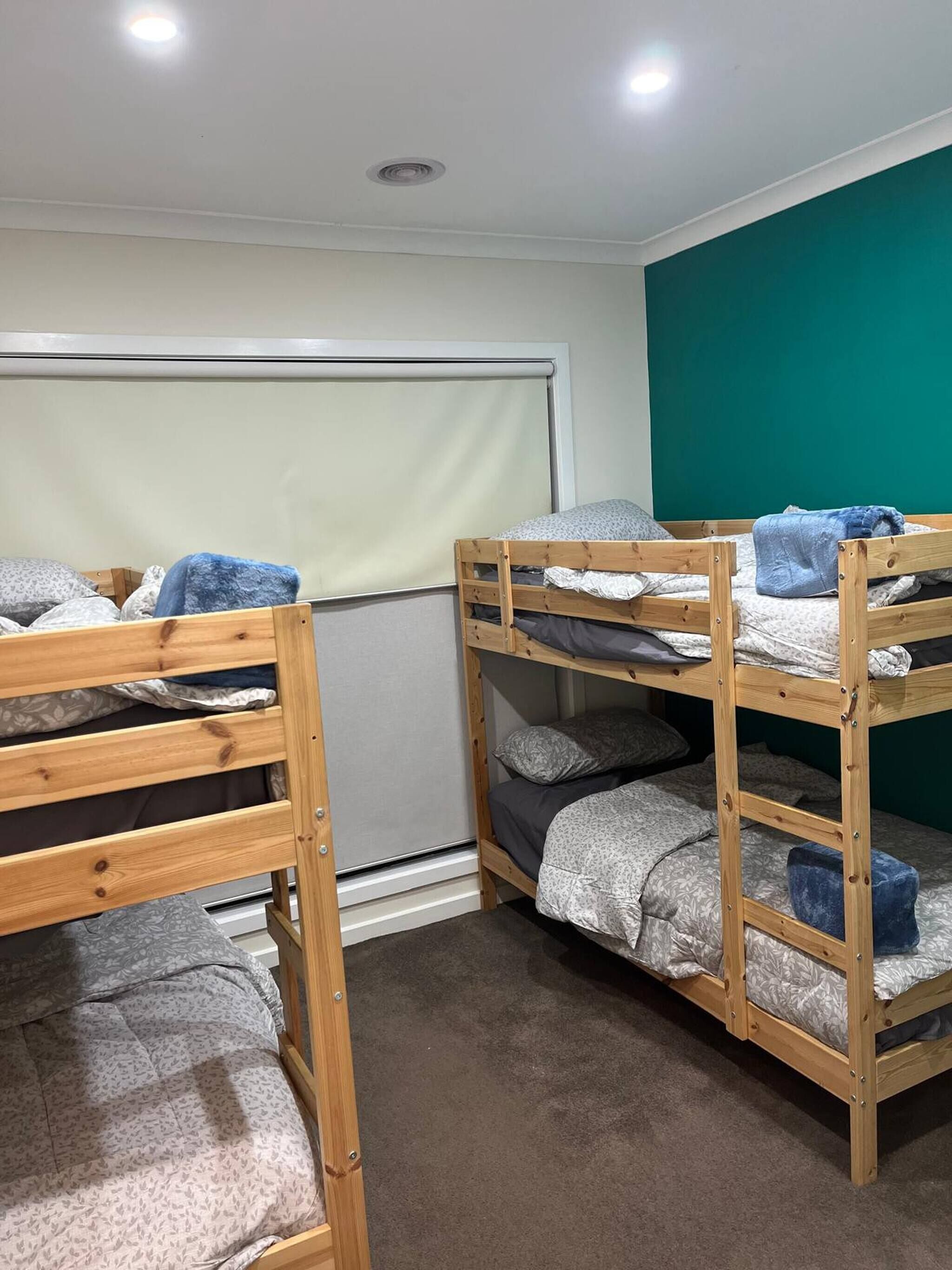 A dormitory room with two bunk beds, a window with blinds, and a teal-colored wall.