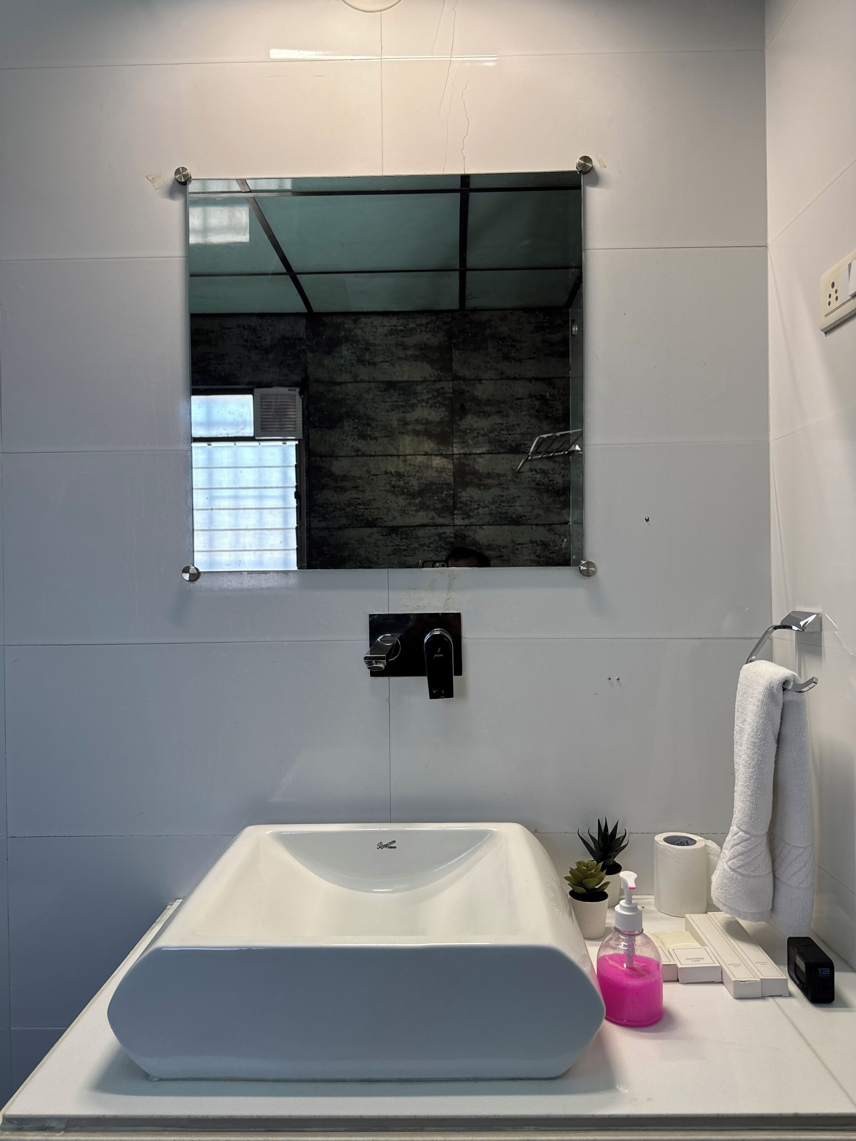 Un baño con un lavamanos grande y rectangular, un espejo, un perchero para toallas, una pequeña planta en maceta y artículos de aseo en la encimera.