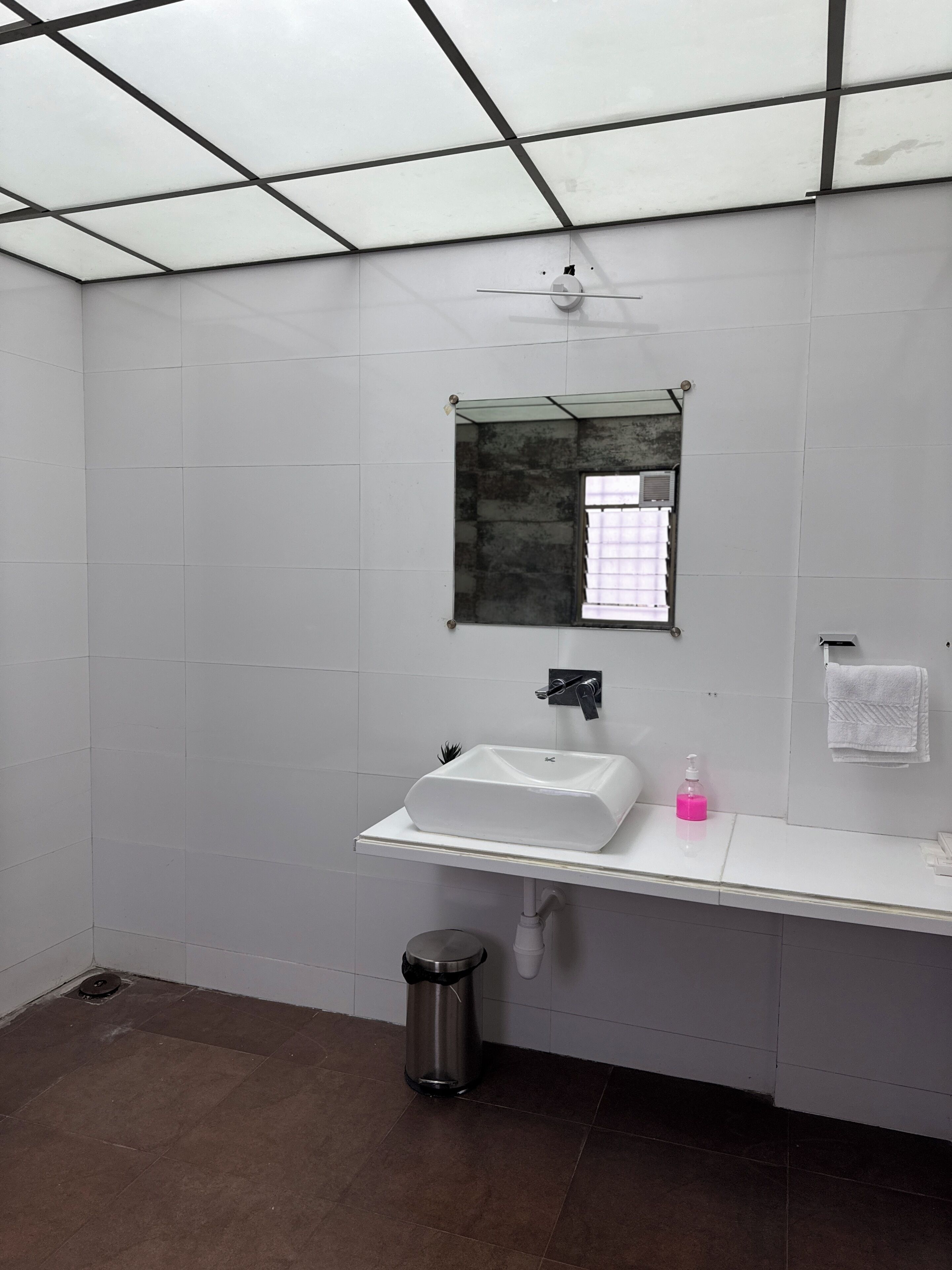 A bathroom with a white sink, a mirror, a trash bin, and a towel rack.