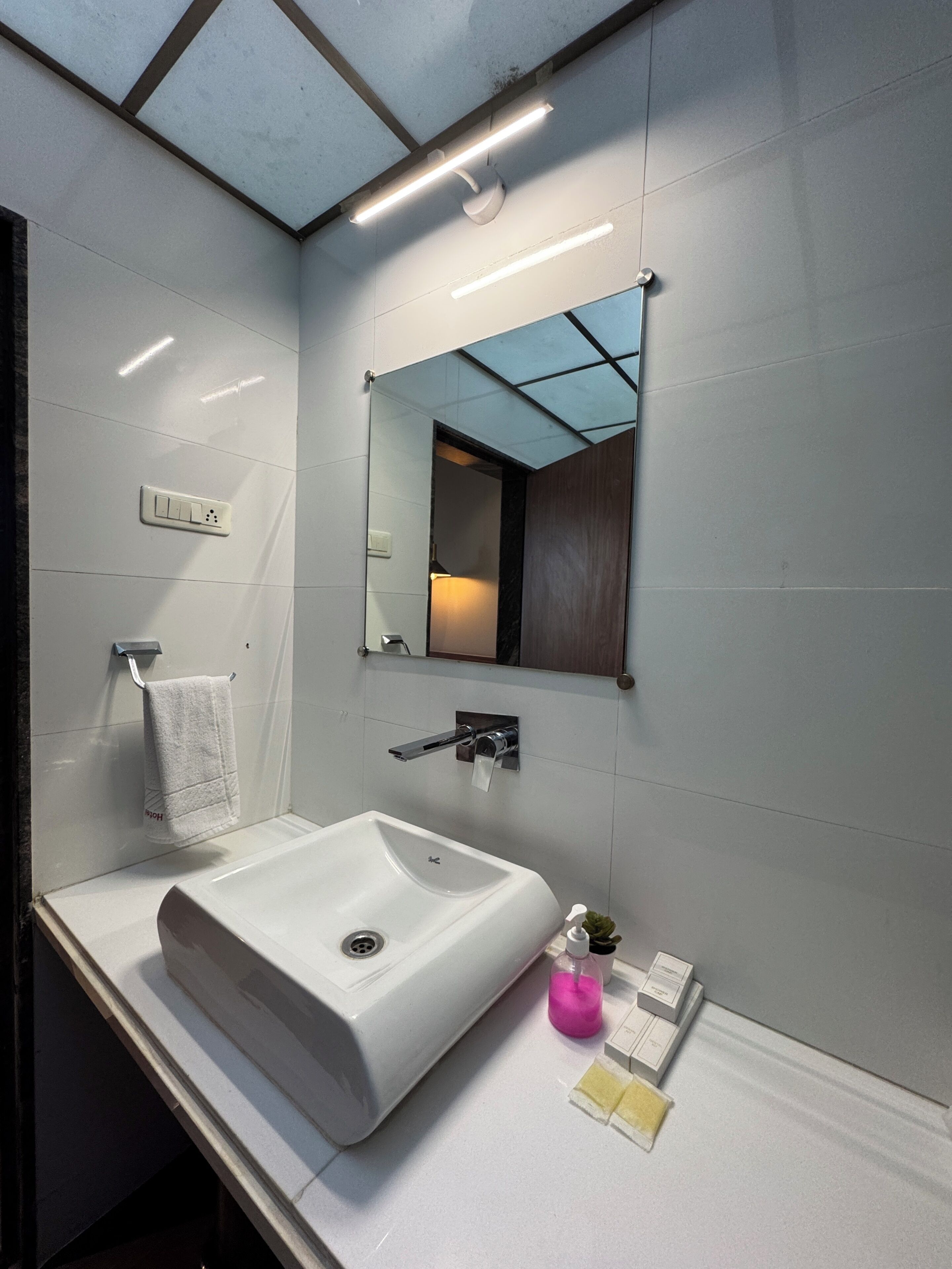 Un baño moderno con un lavamanos blanco, un espejo y un perchero para toallas.
