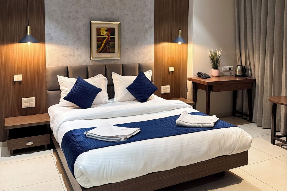 Una camera d'albergo moderna con un letto grande, due comodini, una ventola a soffitto, un quadro appeso e un tavolino con una pianta e un bollitore.