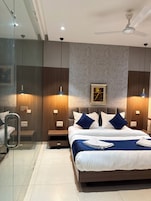 Una habitación de hotel moderna con cama, mesitas de noche, ventilador de techo y una obra de arte enmarcada en la pared.