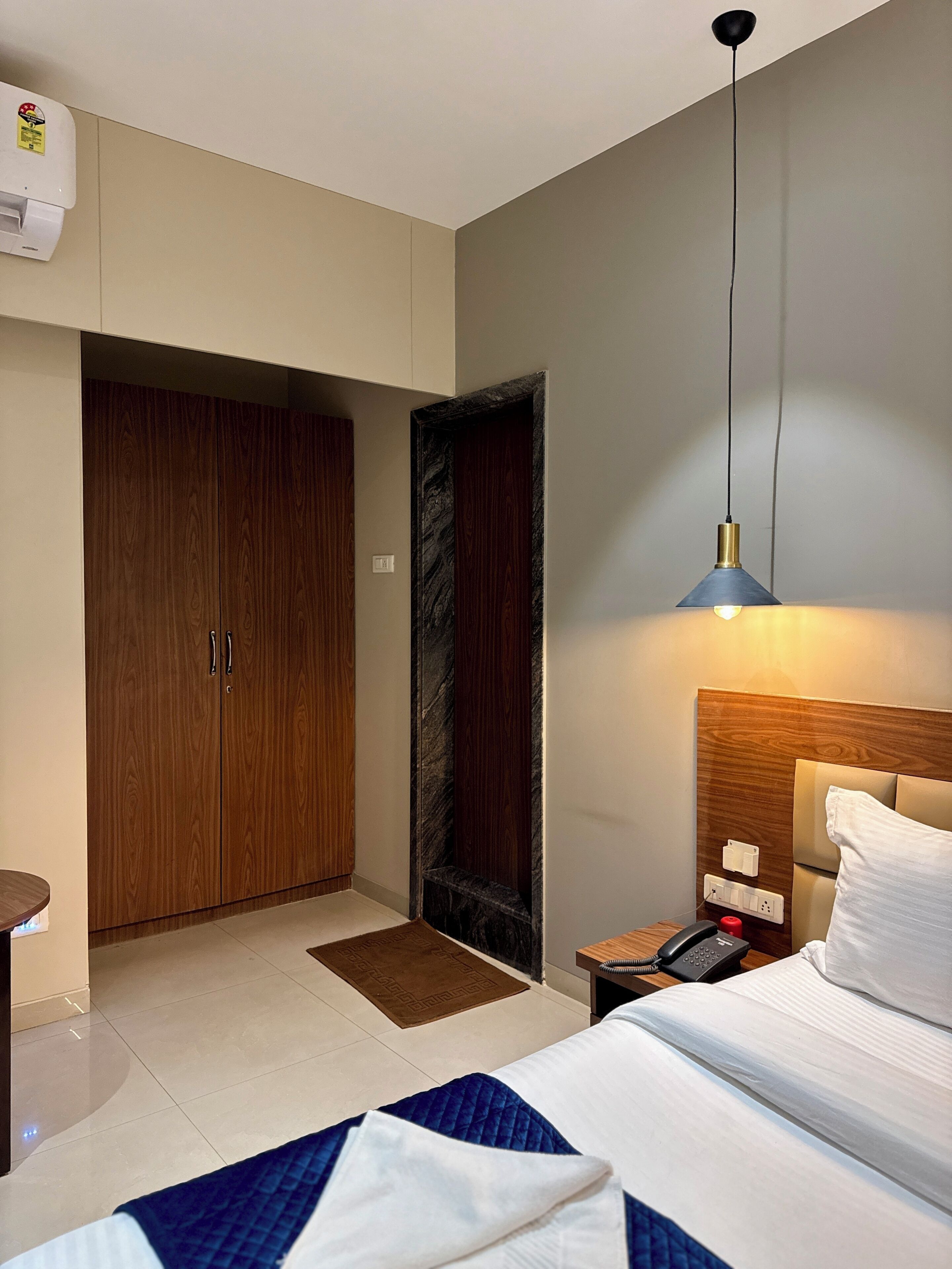 A hotel room with a bed, bedside table, lamp, wardrobe, and a door.
