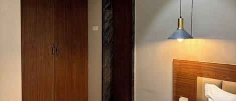 A hotel room with a bed, bedside table, lamp, wardrobe, and a door.