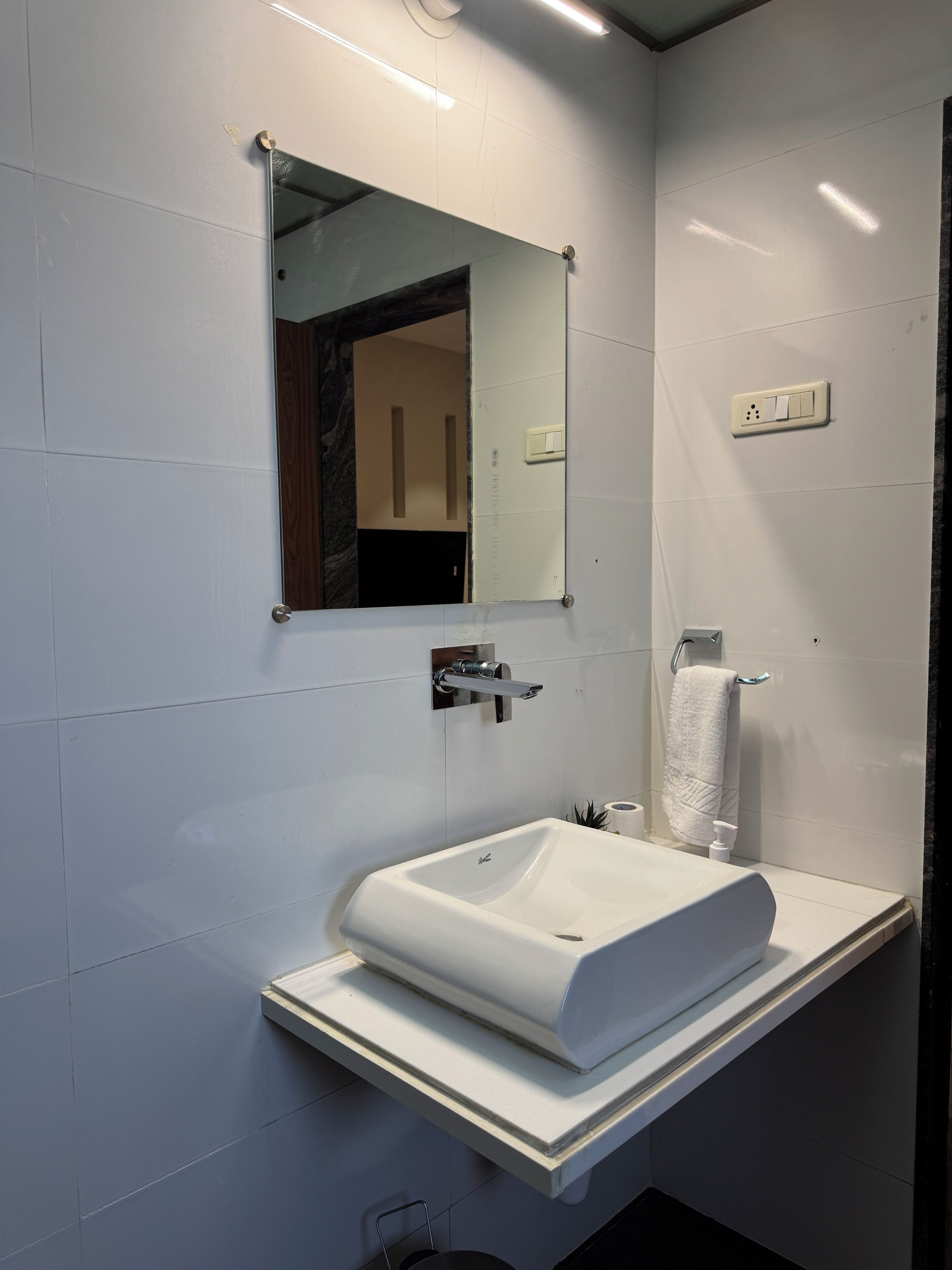 A bathroom with a white sink, a mirror, a towel rack, and a toilet paper holder.