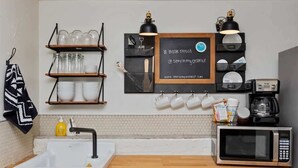 A kitchen with a white sink, wooden countertop, and a black and white patterned towel. There are shelves with glassware and a chalkboard with text. - #StayInMyDistrictTwin Falls Monthly Furnished (Twin Falls)