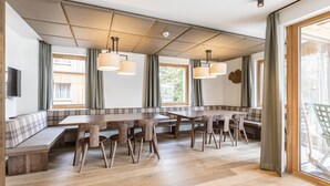 A modern dining area with wooden tables and benches, large windows with curtains, and pendant lighting. - Premium Lodge With Sauna (Hermagor-Pressegger See)