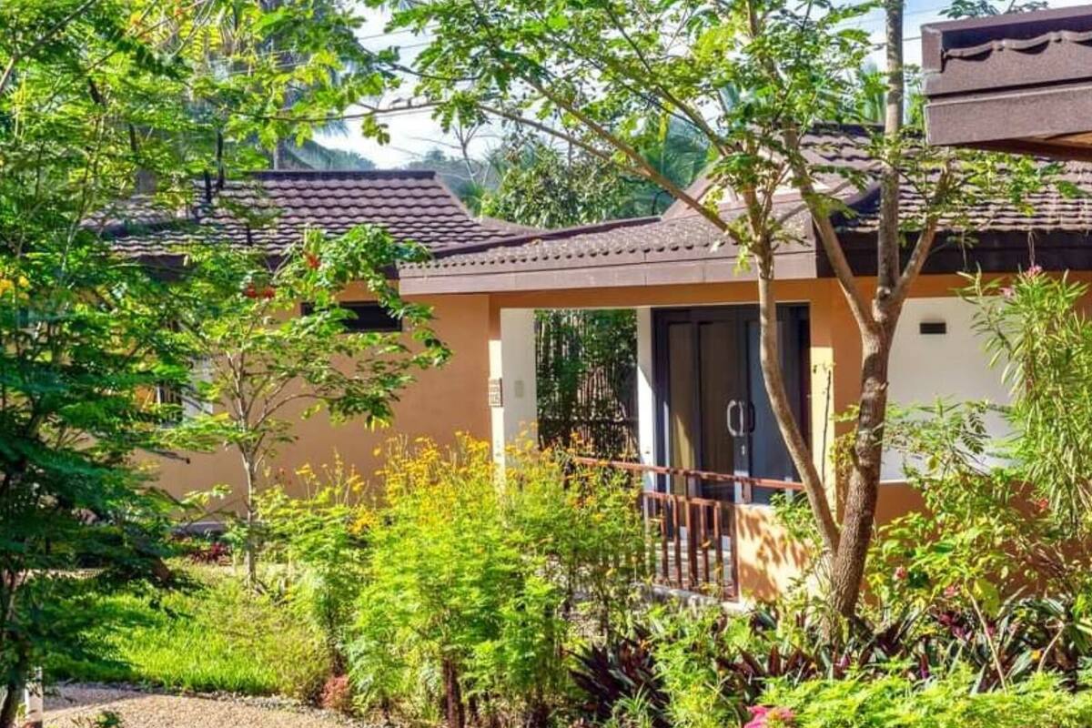 Un edificio con techo de tejas, un pequeño porche y un jardín con diversas plantas y flores.