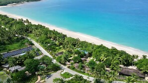 An aerial view of a coastal area with a beach, lush greenery, and a solar panel array. - Dianao Beach Club and Resort (Casiguran)