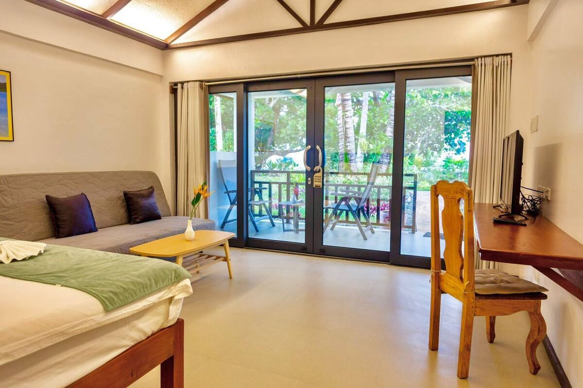 Una habitación con cama, sofá, una silla de madera, una mesita y un balcón con sillas y una mesa.