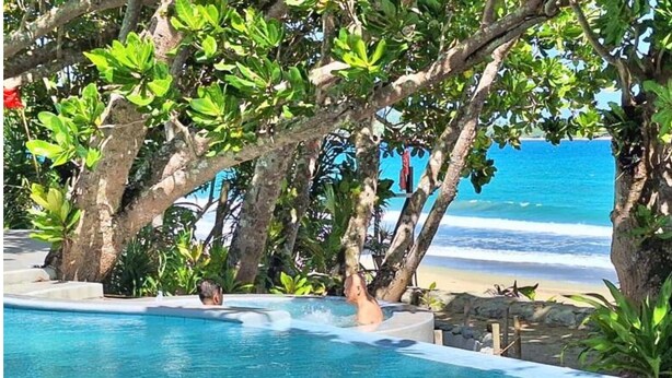 A clear blue pool with a person in the water, surrounded by lush greenery and overlooking a beach. - Dianao Beach Club and Resort (Casiguran)