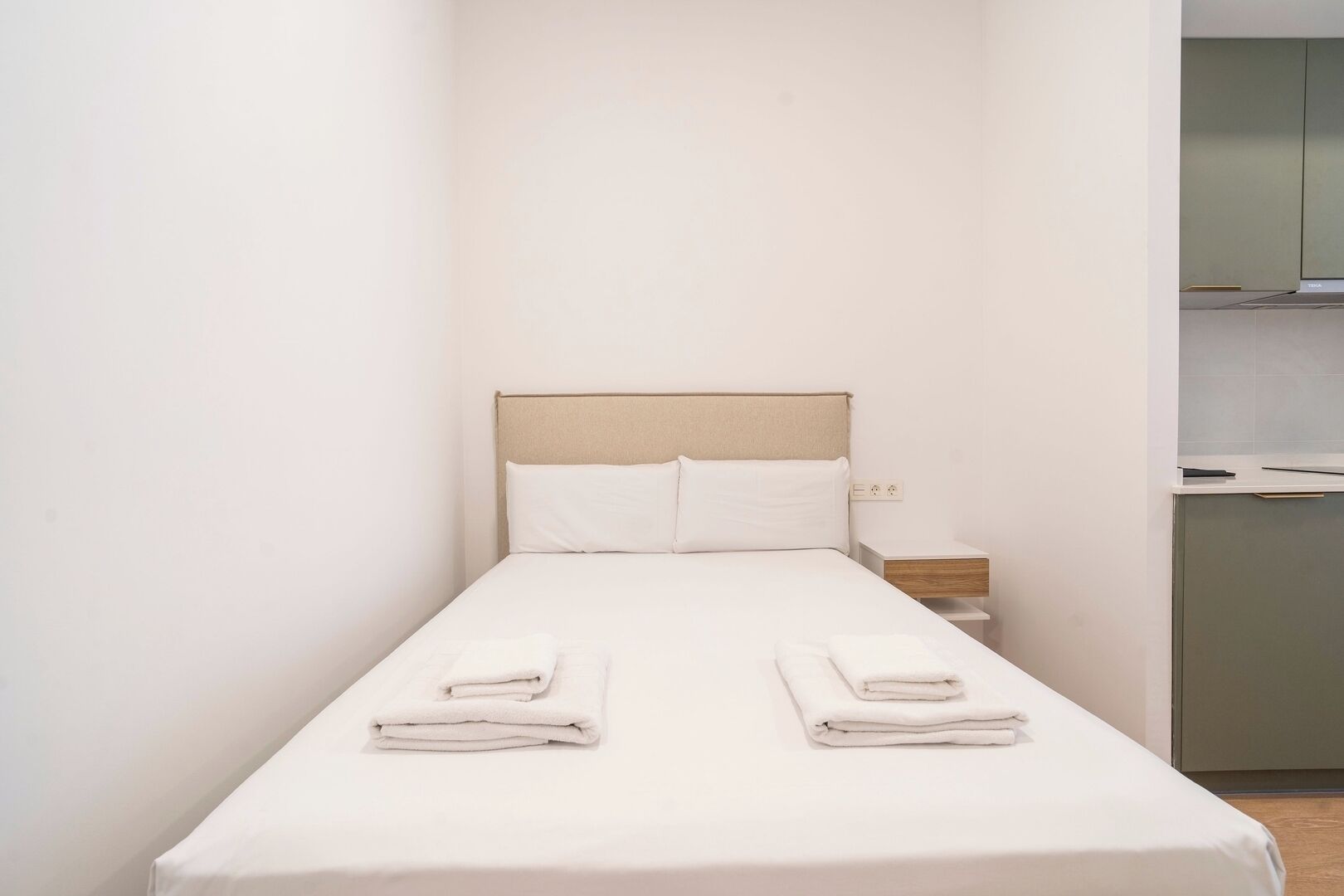 A small, single-bed room with a beige headboard, white bedding, and two neatly folded towels on the bed.