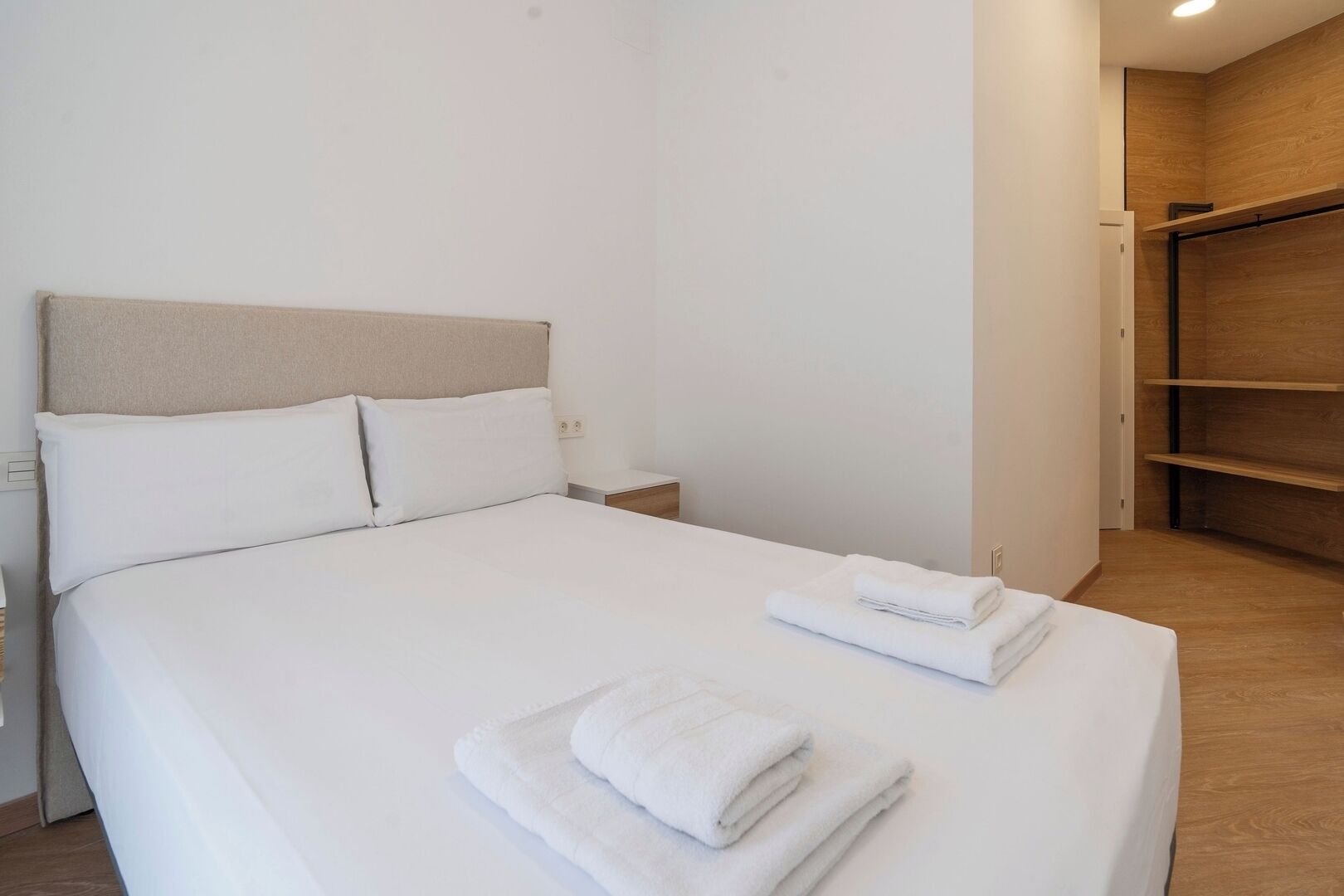 Un lit bien fait, avec du linge de lit blanc et des serviettes pliées, une tête de lit en bois et une armoire en bois, dans une chambre moderne au style minimaliste.