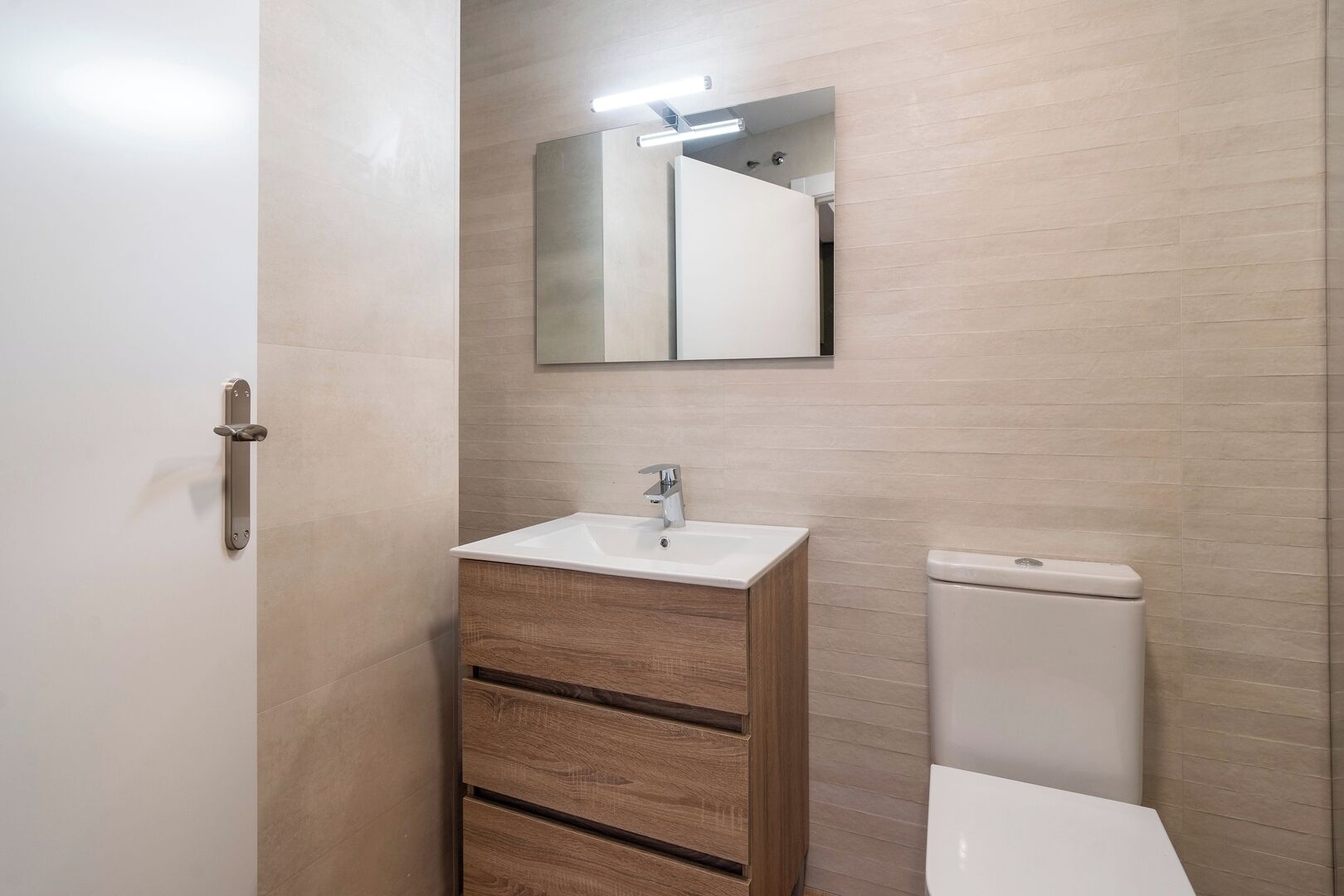 A bathroom with a white sink, wooden cabinet, and a toilet.