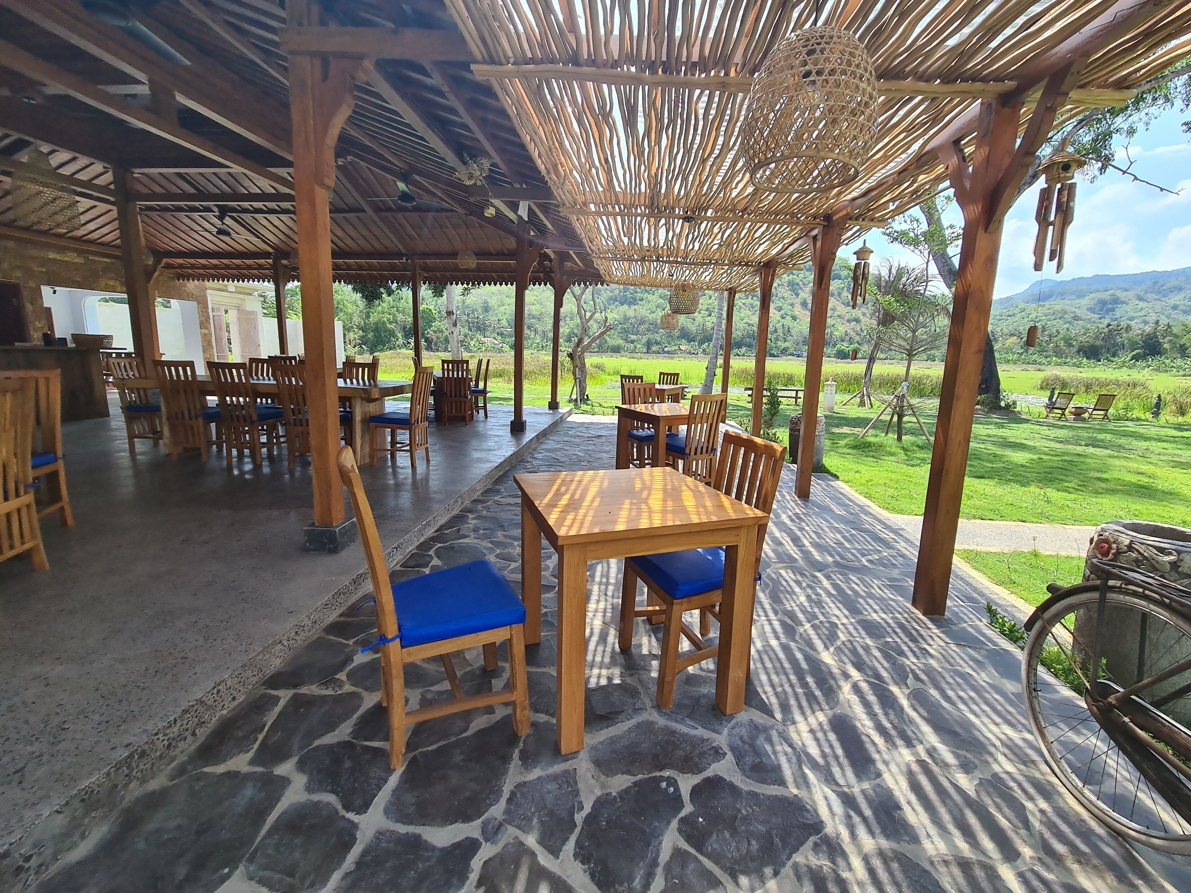 A covered outdoor dining area with stone flooring and wooden furniture.