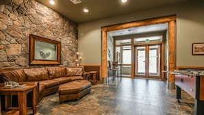 A lobby with a stone wall, leather sofa, wooden table, and a foosball table. - Arapahoe Lodge 8102 OFB (Keystone)