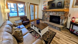 A living room with a stone fireplace, leather sofa, and a coffee table. - Arapahoe Lodge 8102 OFB (Keystone)