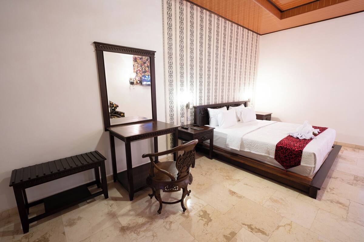 A hotel room with a bed, a wooden desk, a chair, and a large mirror.