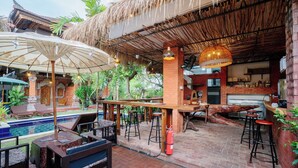 Un área de bar al aire libre con piscina, sillones de descanso y techo de paja.