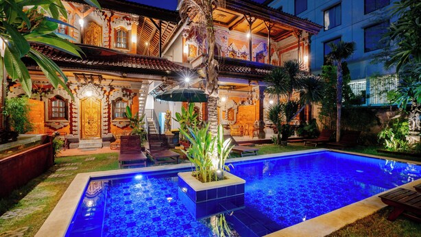 Una piscina con un diseño de mosaicos, rodeada por un jardín cuidado y un edificio de arquitectura tradicional.
