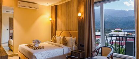 A hotel room with a bed, bedside table, chair, and a view of mountains.
