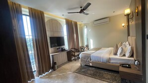 A modern hotel room with a bed, a desk, a TV, and a ceiling fan. - HOTEL HRISHIKESH HIGH (Rishikesh)