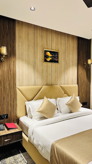 Habitación de hotel con pared de paneles de madera, cama con ropa de cama blanca y beige, dos lámparas de noche y mesita de noche con un teléfono y un libro rojo.