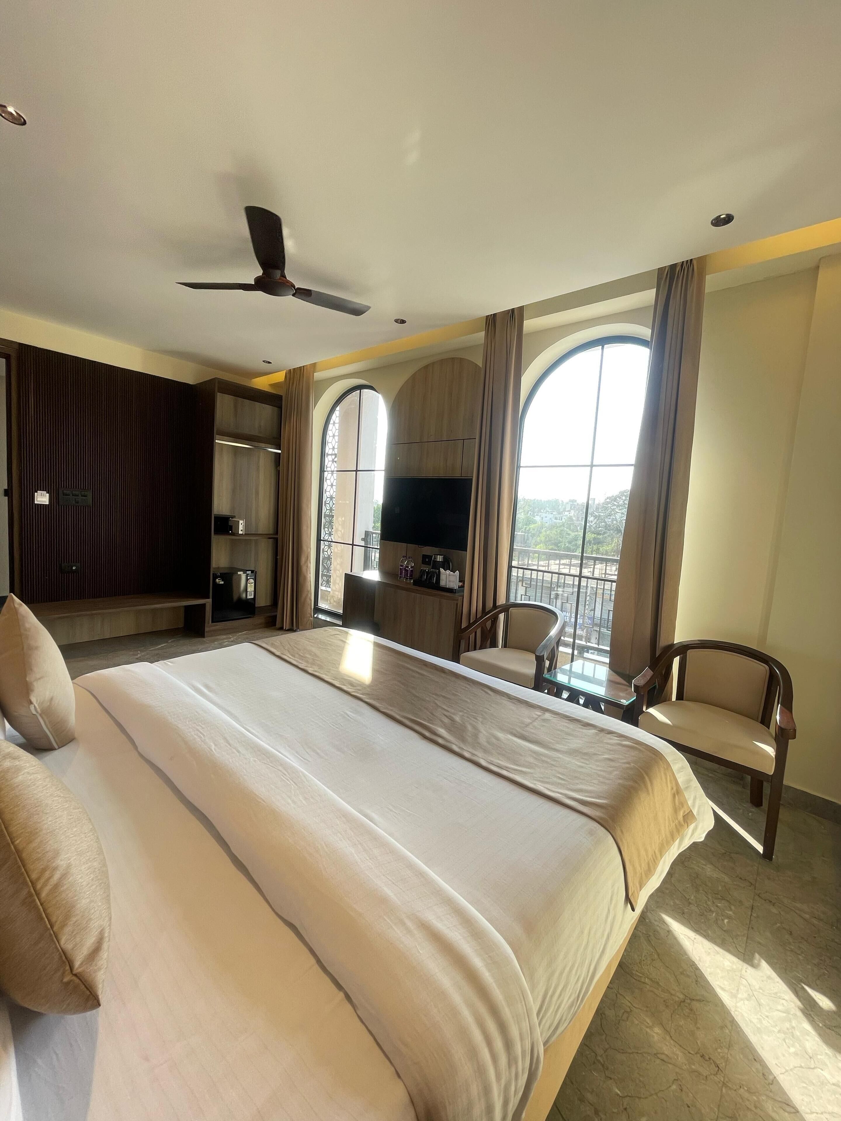 A hotel room with a large bed, a desk with a flat-screen TV, a chair, and a balcony with a view.