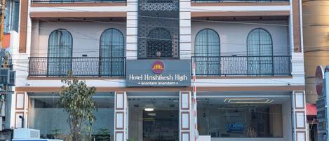 Et hotel med flere etager, moderne facade, altaner og et skilt, der angiver, at det er Hotel Hrishikesh High.
