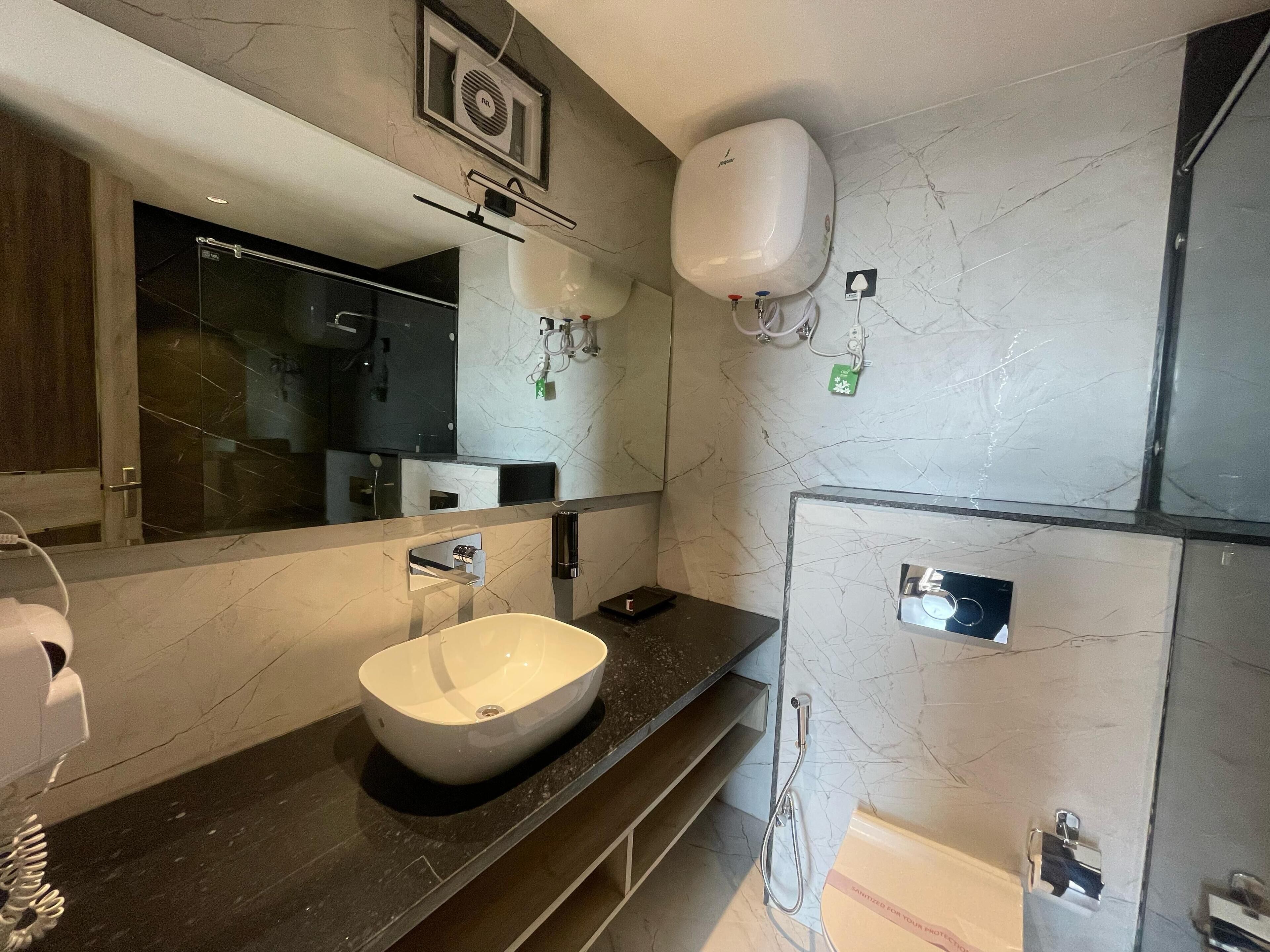 A modern bathroom with a large mirror, a vessel sink, a handheld showerhead, and a toilet with a privacy partition.