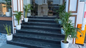 A set of black marble steps leading to a glass door entrance, flanked by white planters with green plants. - HOTEL HRISHIKESH HIGH (Rishikesh)