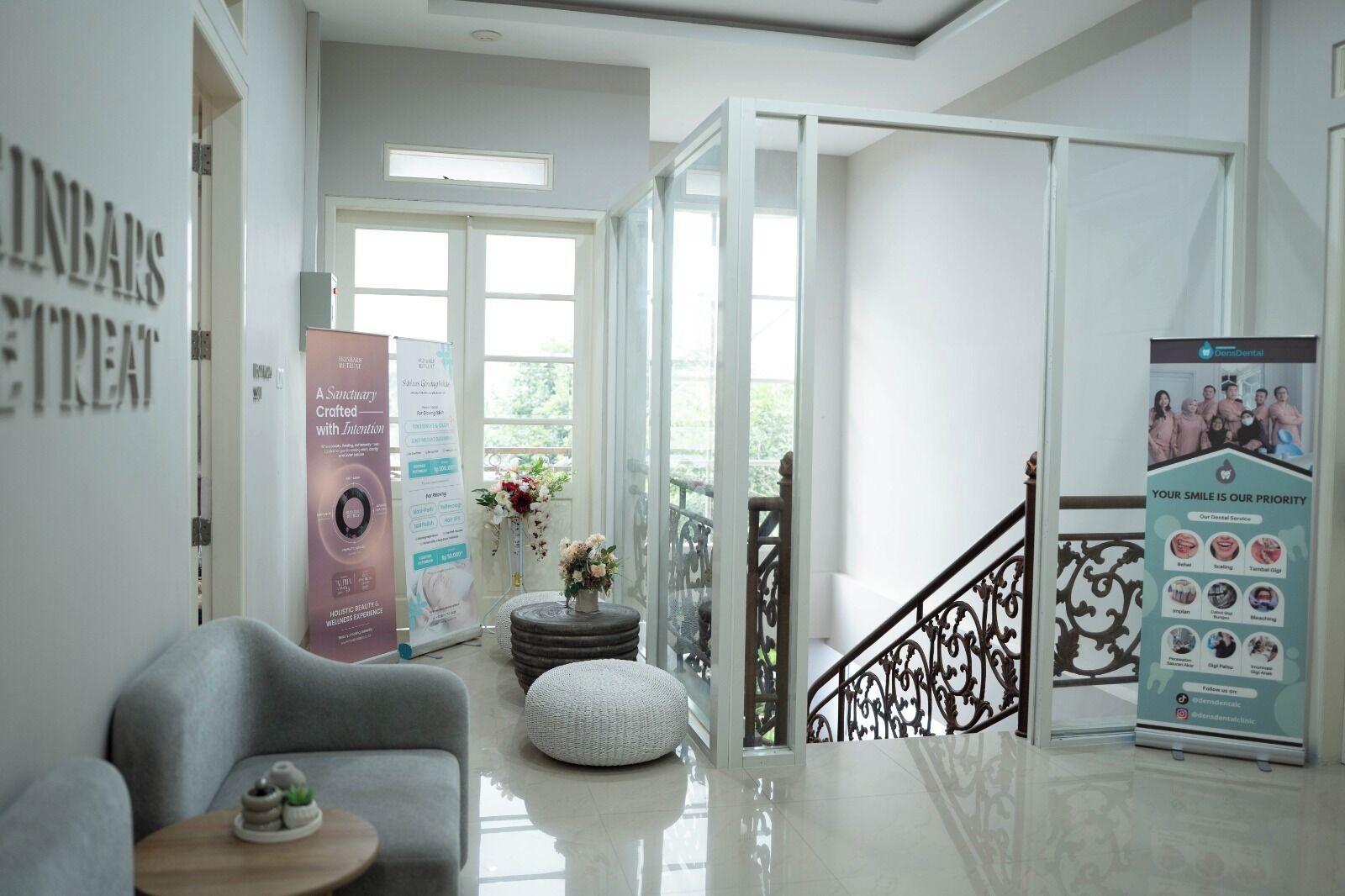 A modern interior with a grey sofa, a round ottoman, a small table with a plant, and a staircase with a metal railing.