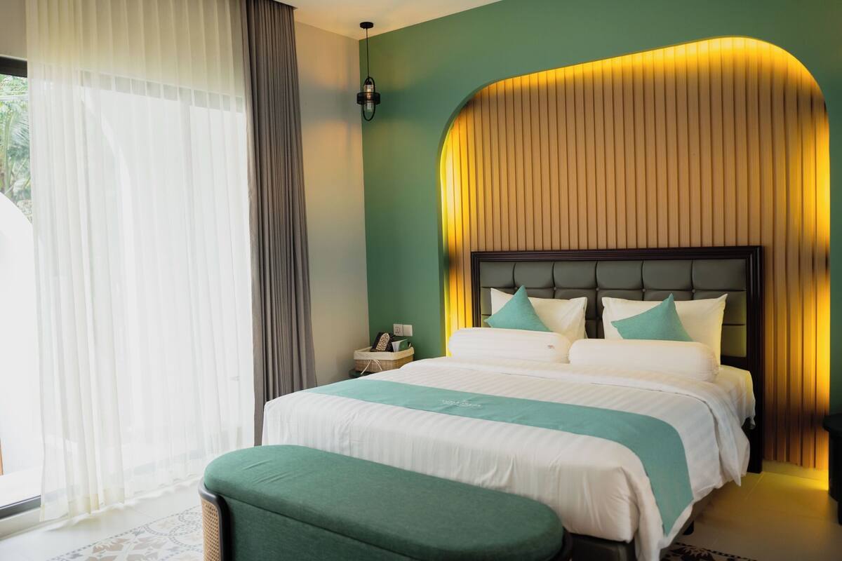 Une chambre d’hôtel avec un grand lit, une table de chevet, une lampe et une vue sur la verdure.