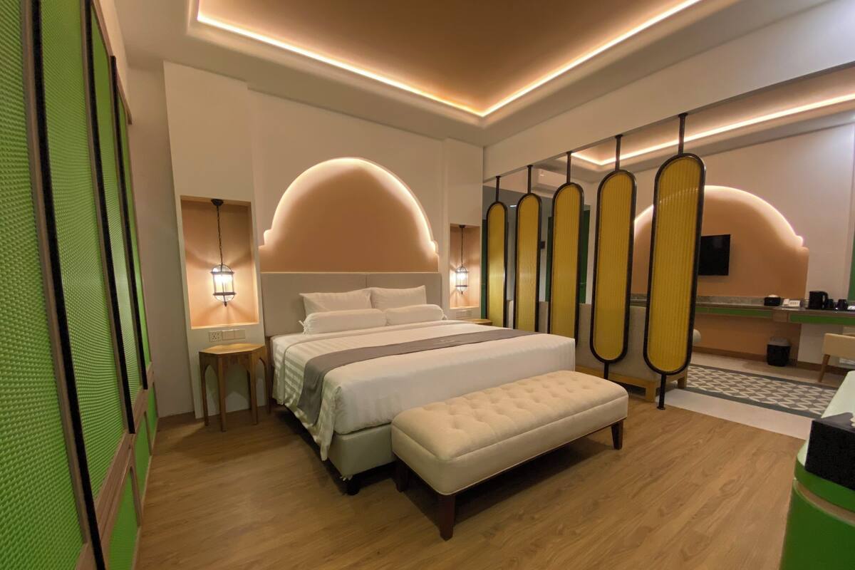 Une chambre d’hôtel moderne avec un grand lit, un banc, une petite table et un coin cuisine.
